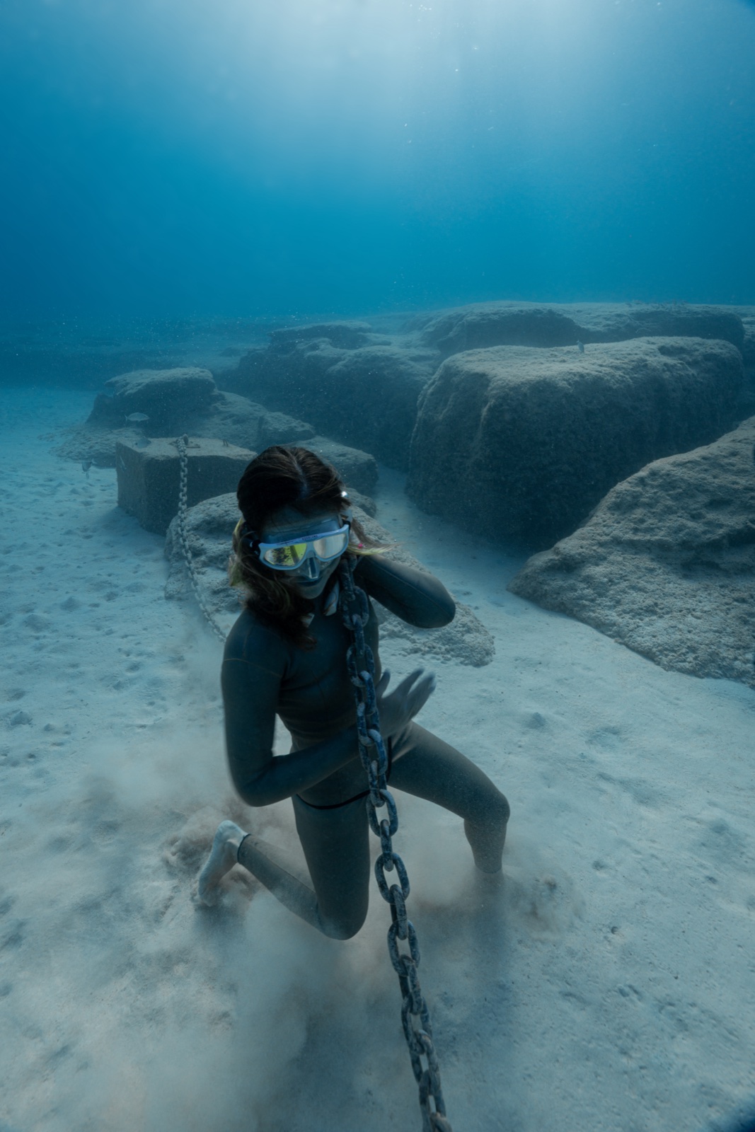 Freediver kneeling beside anchor chain on white sand Mediterranean apnea