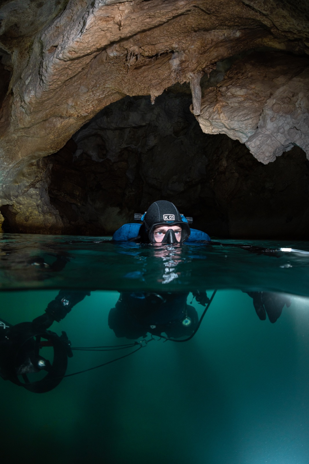 GUE cave diver split shot at cavern surface, half above half below water